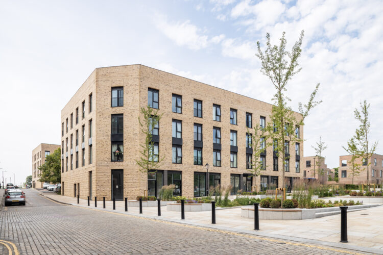 A tree-lined path between beautiful brick buildings, showcasing Bolton's charming architecture on a sunny day.