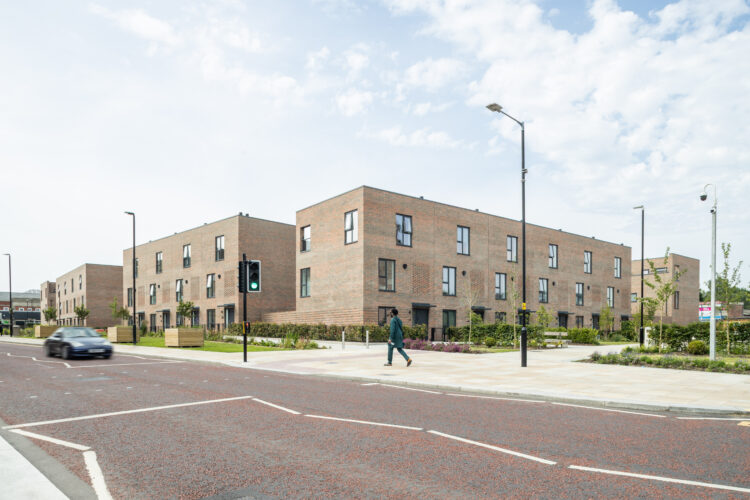 A tree-lined path between beautiful brick buildings, showcasing Bolton's charming architecture on a sunny day.