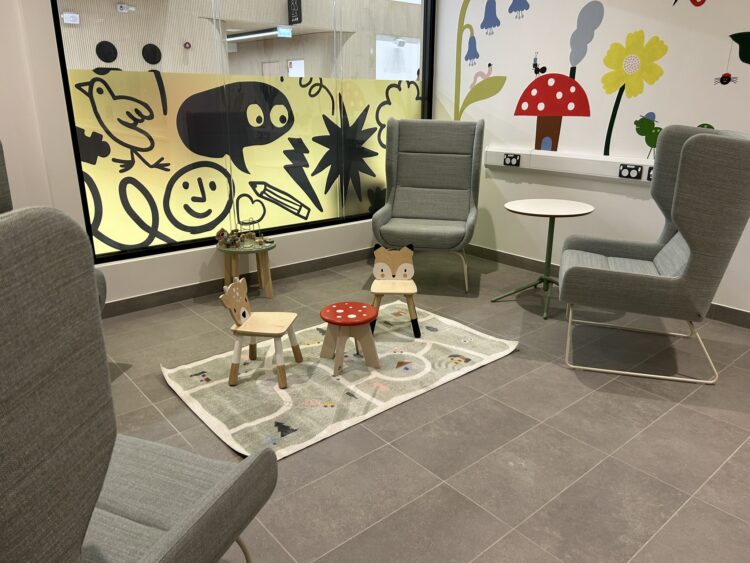 Stockroom in Stockport with bright and playful waiting area featuring modern grey lounge chairs, a children’s seating corner with animal-themed stools, and colourful wall graphics creating a welcoming family-friendly environment. Designed by AEW Architects.