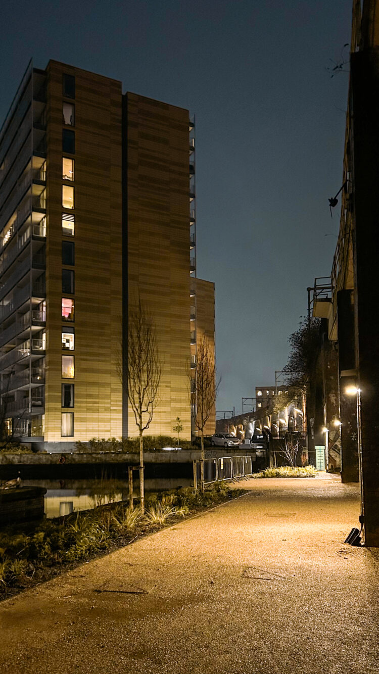 View out over the public realm and neighbouring canal at Embassy Village. Apartment blocks and the night sky sit in the background.